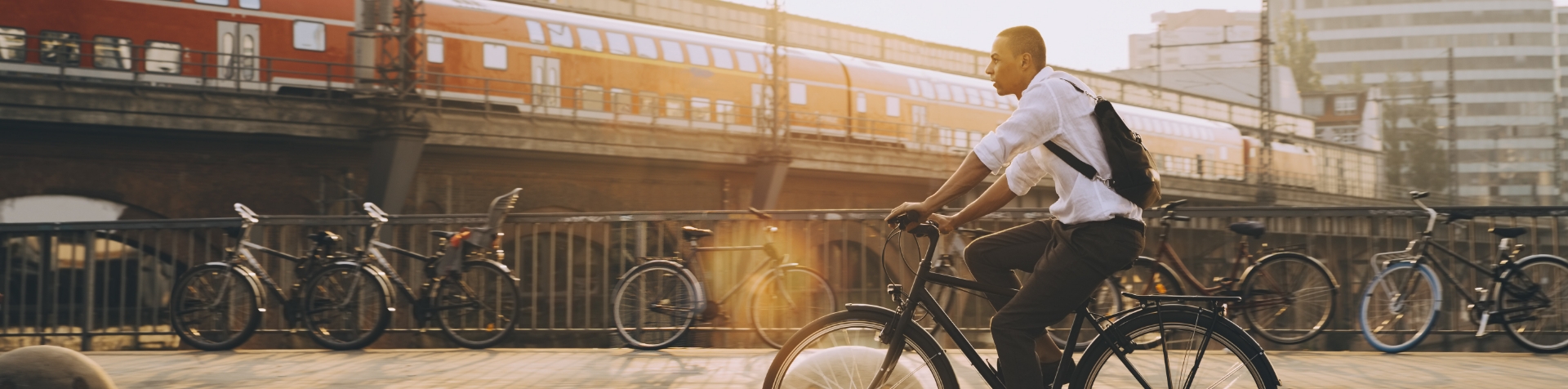 A guy riding a bicycle with a backpack on a sunny day. Many bicycles are in the background.