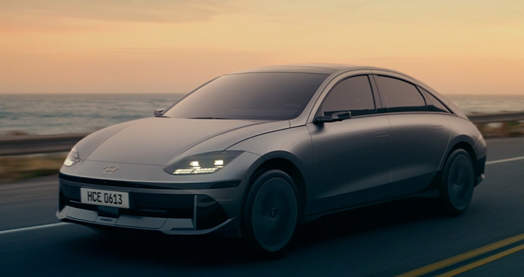 The front of a silver Hyundai IONIQ 6 driving along a coastline at sunset. 