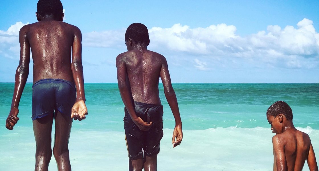 Three Senegalese boys wearing shorts, all lined up and ready to jump into the ocean.