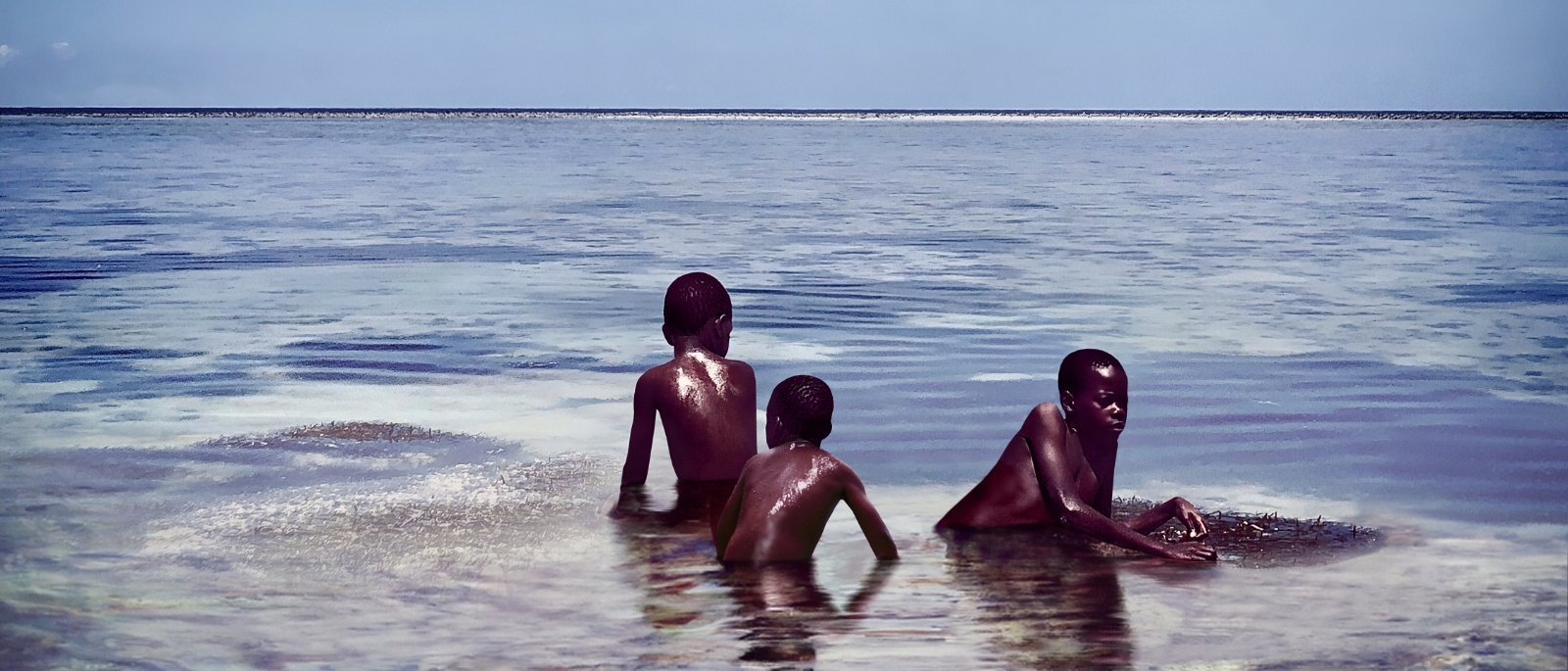 Three boys sitting on the last remaining piece of land surrounded by ocean. 